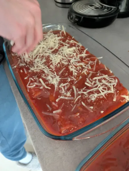 Geriebener Eatlean Käse wird von Hand über die mit Tomatensoße bedeckten Cannelloni gestreut