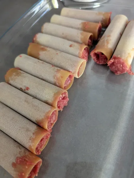 Rohe Cannelloni-Röhren mit Rinderhack gefüllt, nebeneinander in eine Glasauflaufform gelegt
