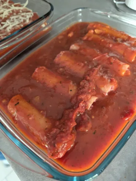 Gefüllte Cannelloni vollständig mit Tomatensoße bedeckt in der Auflaufform vor dem Backen