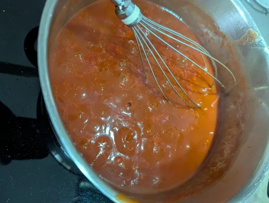 Tomatensoße aus passierten Tomaten und Brühe wird im Topf mit dem Schneebesen glatt gerührt