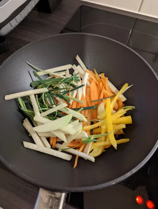 Rohe Gemüsestreifen im Wok: Sellerie, Karotte, gelbe Paprika, Zwiebel und grüner Porree