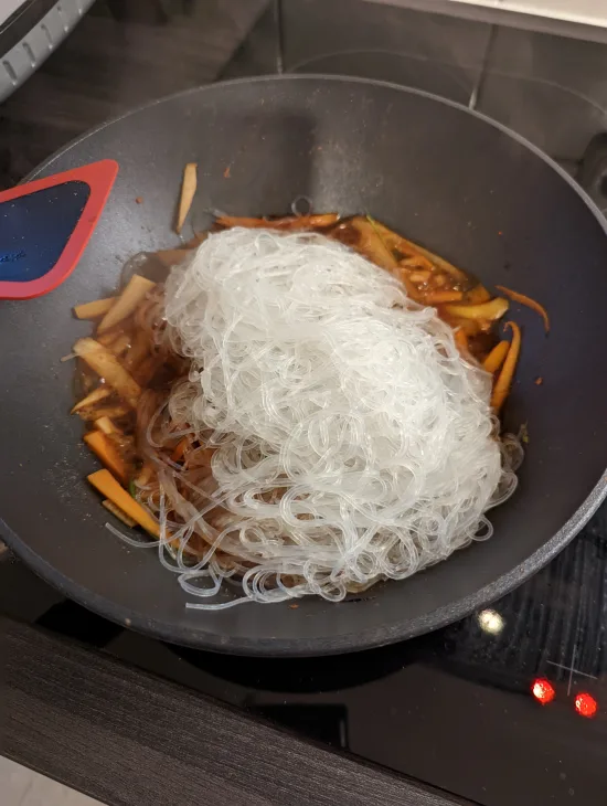 Die abgetropften Glasnudeln werden auf das Gemüse in den Wok gegeben