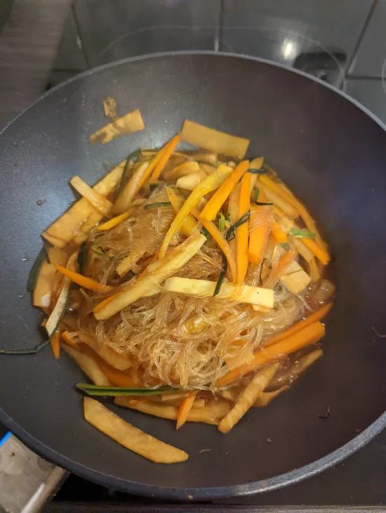 Glasnudeln und Gemüse sind im Wok vermischt und gleichmäßig von der Sauce überzogen