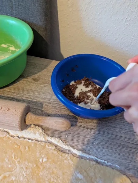 Milch wird zu gemahlenen Haselnüssen, Zucker und Semmelbröseln in eine blaue Schüssel gegossen
