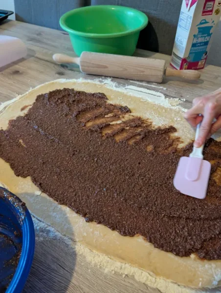 Nussfüllung wird mit einem Teigschaber auf den ausgerollten Hefeteig gestrichen