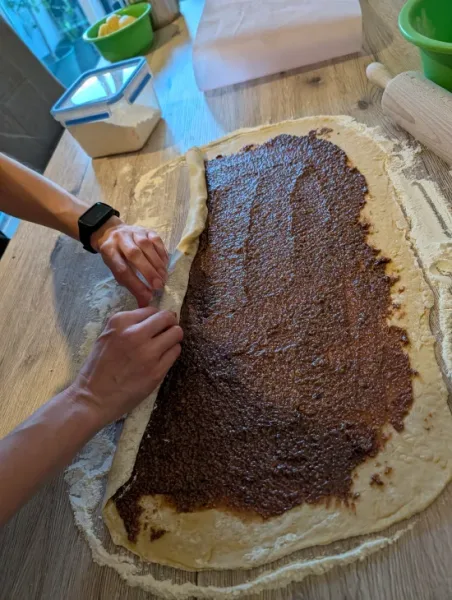 Der mit Nussfüllung bestrichene Teig wird von der Längsseite her aufgerollt