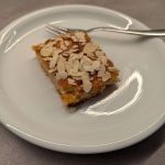 Ein Stück saftiger Apfel-Marzipan-Kuchen mit gehobelten Mandeln auf einem weißen Teller, bereit zum Servieren.