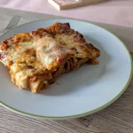 St&uuml;ck Lasagne mit Rinderhackfleisch und geschmolzenem Mozzarella auf wei&szlig;em Teller, die Schichten aus Nudelplatten und Tomatensauce sind im Anschnitt sichtbar