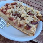 St&uuml;ck Pflaumenkuchen mit Hefeteig und Butterstreuseln auf einem wei&szlig;en Teller