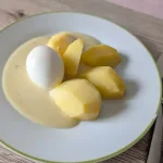 Gepelltes hart gekochtes Ei mit Salzkartoffeln in heller Senfso&szlig;e auf einem Teller
